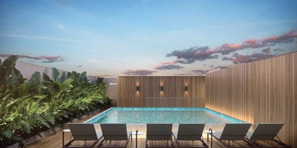 Guilhem Mozak Leblon - Vista ampla do rooftop com piscina e espreguiçadeiras, cercado por vegetação tropical e cercado por prédios do Leblon ao fundo.