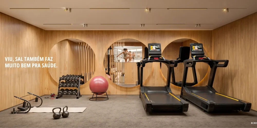 Academia moderna do Sal Praia Ipanema com esteiras, área funcional e design em madeira, iluminação quente e ambiente sofisticado.